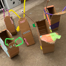 Load image into Gallery viewer, A group of handmade cardboard snails decorated with colorful tape, pipe cleaners, googly eyes, and small paper accents, arranged on a concrete floor.